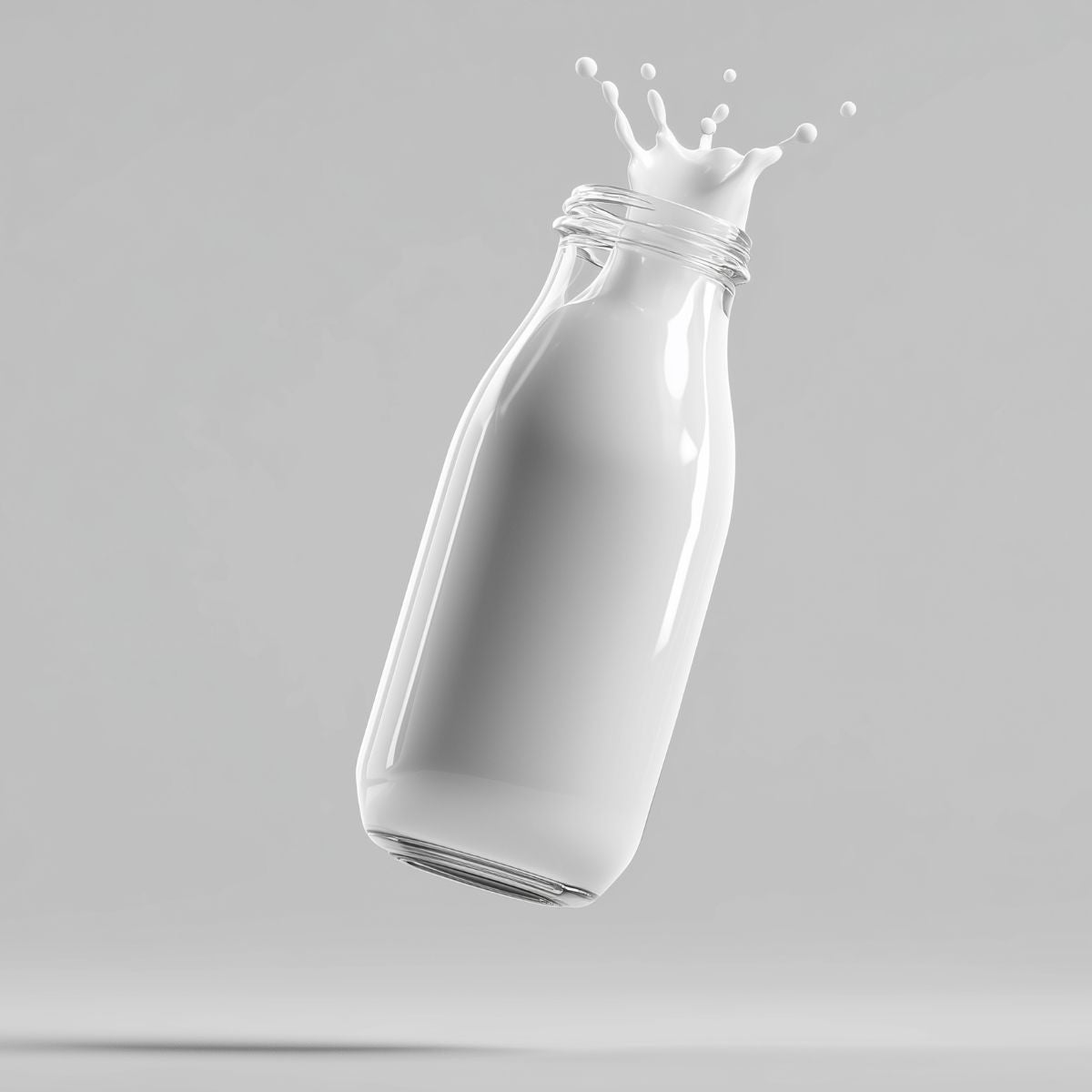 Clear glass bottle with milk splashing out on a gray background